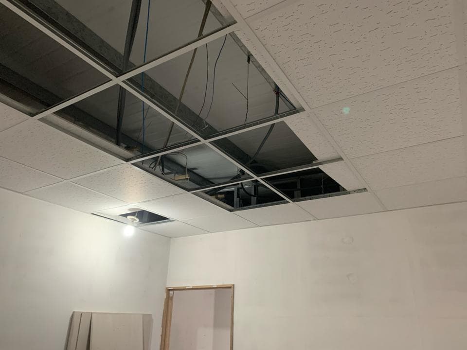 1) 照片顯示一個正在施工的房間,天花板上有幾塊已安裝的白色天花板,但有些部分尚未安裝,呈現出黑色的洞口