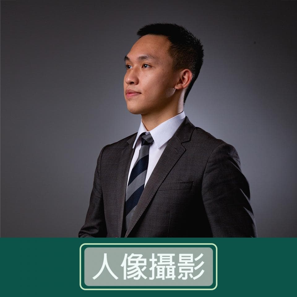 這張「人像攝影」的照片是一個穿著西裝的男士,他站在灰色背景前,眼神堅定。