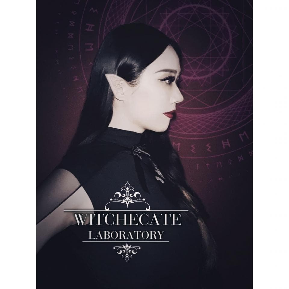 這張照片是一個年輕女人,她穿著黑色的衣服,戴著精緻的耳環。她的背景是魔法符號,上面寫著 "WITCHGATE LABORATORY"。