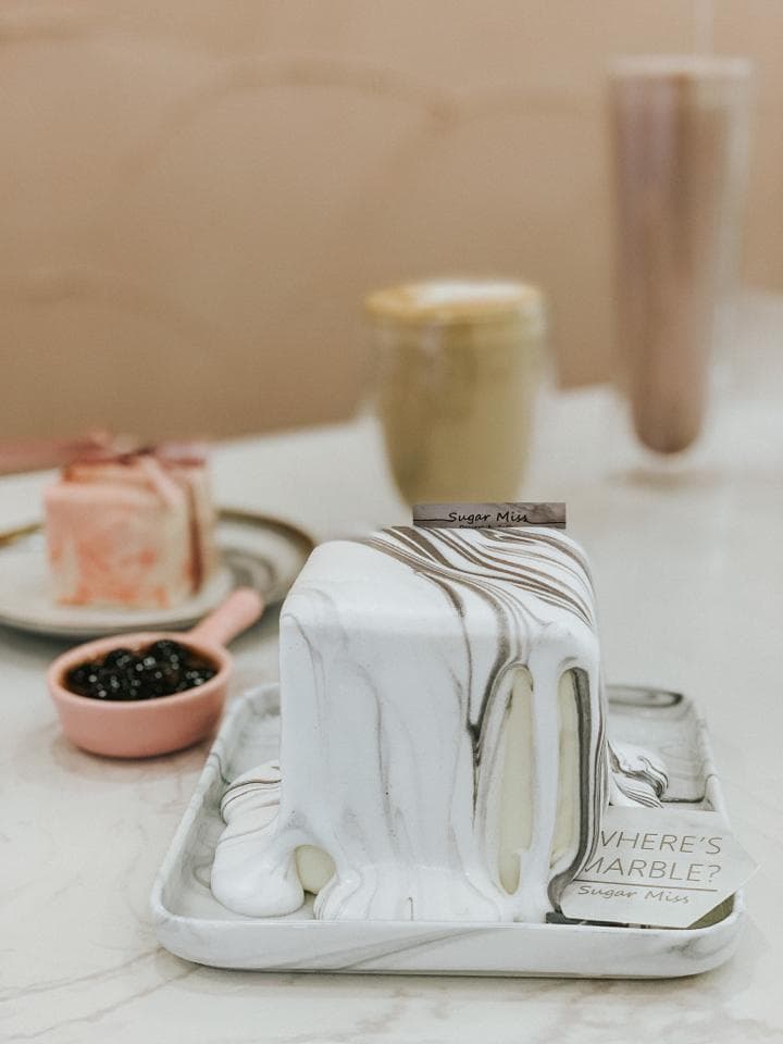 這張「甜點」的照片是一個以白色和灰色大理石紋路裝飾的蛋糕,旁邊放著一杯咖啡和一盤珍珠奶茶。蛋糕看起來很美味,而且很漂亮。