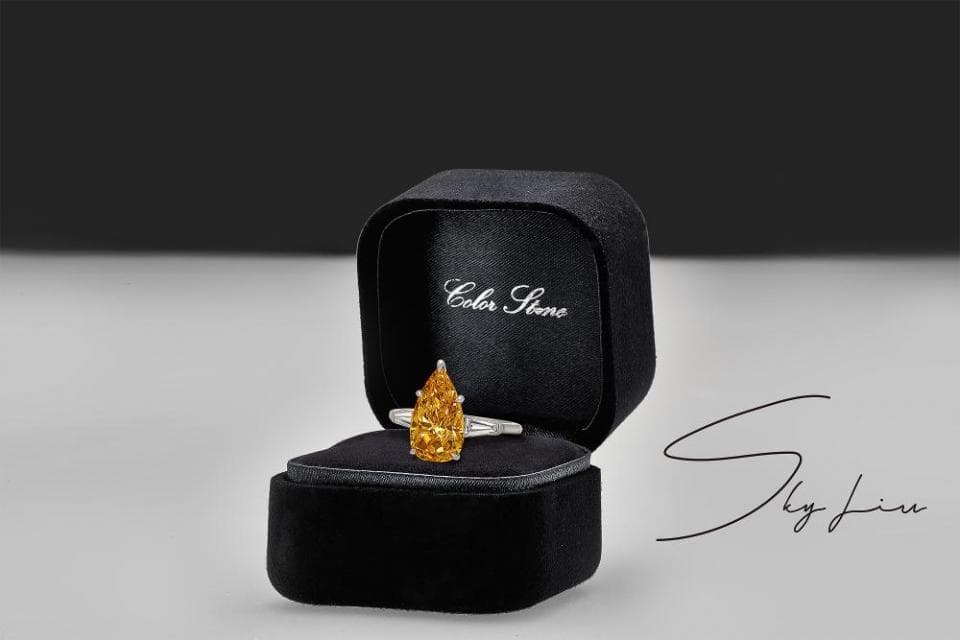 這張照片是一枚黃色梨形鑽戒,放在一個黑色的首飾盒裡。