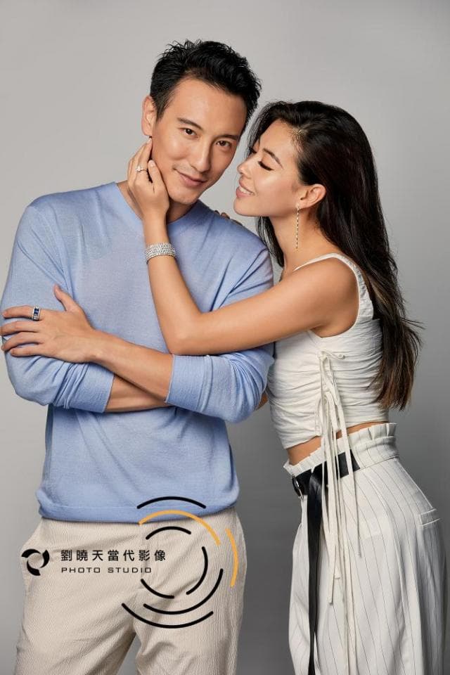 這張照片是一對情侶的親密合影。男的穿著淺藍色毛衣,女的穿著白色上衣和米白色褲子,他們彼此依偎著,男的用手輕輕地撫摸著女子的臉頰,女子的手搭在男的肩膀上,他們的眼神充滿了愛意,給人一種溫馨甜蜜的感覺。