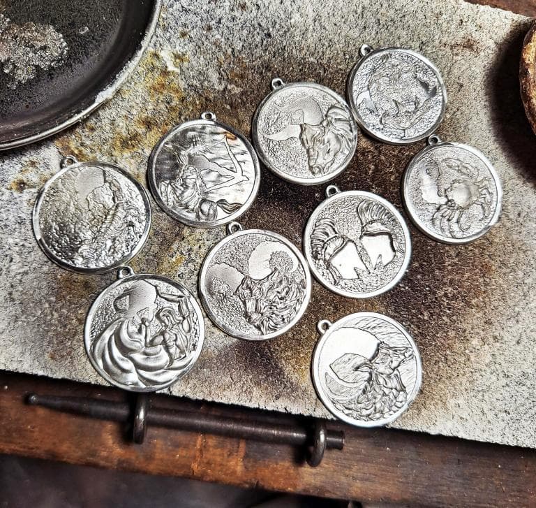 1) 照片中顯示十個銀色圓形吊墜,每個吊墜上都刻有不同的圖案,這些吊墜看起來像是手工製作的