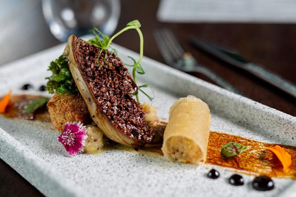 這張「美食」的照片是煎香的鵝肝,上面淋著醬汁,旁邊搭配捲起的春捲,以及鮮豔的綠色蔬菜和粉紅色花朵,看起來非常美味。