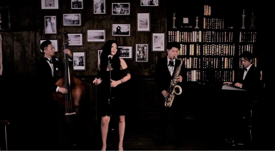 這張照片是一個爵士樂團在一個裝飾著許多照片的房間裡演奏。照片中最重要的是三位音樂家,他們正在演奏不同的樂器:低音提琴、薩克斯風和麥克風。
