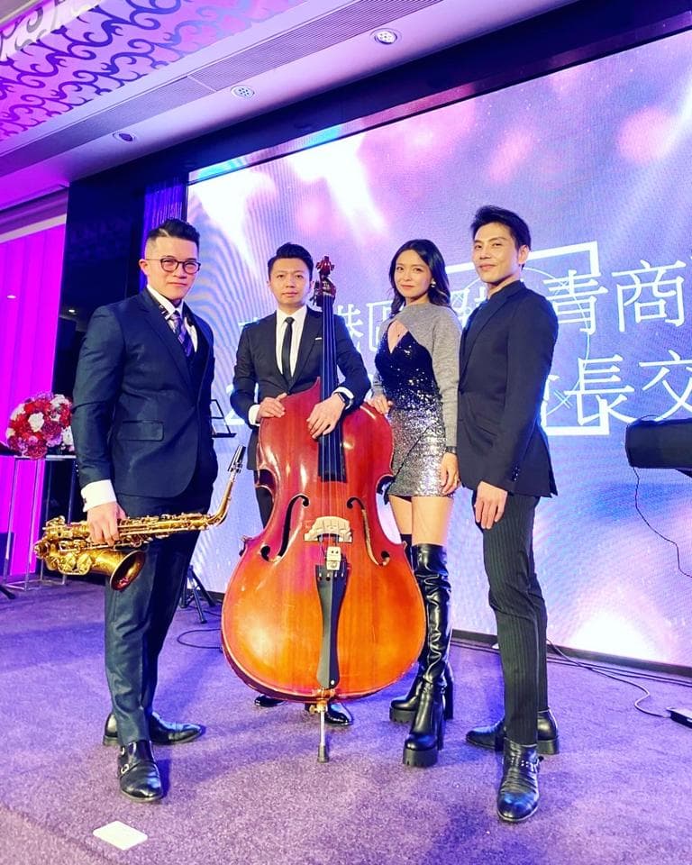 這張照片是一組樂團在舞台上表演,樂團成員包括一位吹薩克斯風的男子、一位拉大提琴的男子和一位穿著黑色連衣裙的女歌手,他們似乎正在為一個婚禮或其他特殊活動演奏。