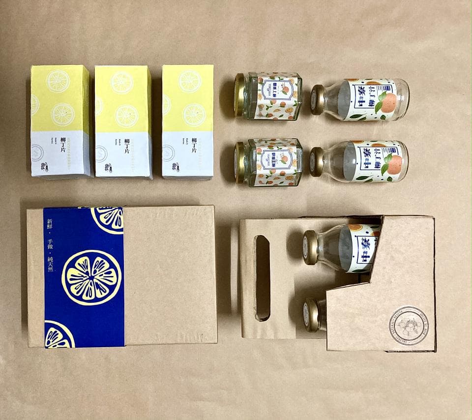 這張照片是四罐裝的檸檬蜂蜜飲品禮盒,禮盒由兩層紙盒組成,上層是四罐裝的蜂蜜飲品,下層是禮盒的內盒。蜂蜜飲品包裝簡單,以黃色和橘色為主,並印有檸檬和蜂蜜的圖案。禮盒外盒的包裝是深藍色,印有檸檬圖案,看起來很精緻。