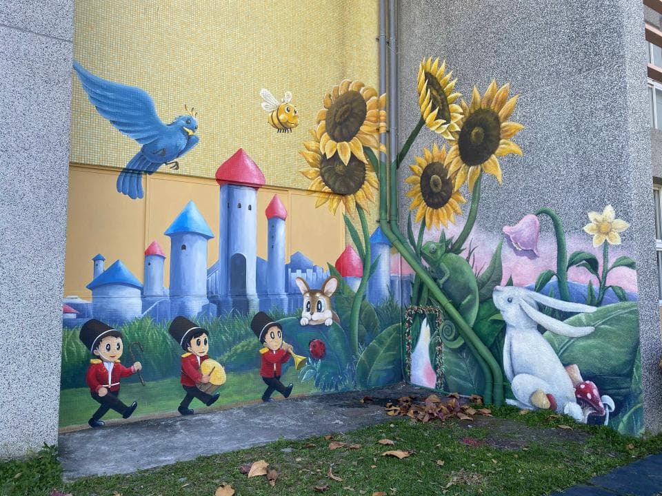 這張「牆壁彩繪」的照片是童話故事主題的,有城堡、小動物、花朵、太陽花等圖案,旁邊還有一些穿著制服的小人,畫面繽紛可愛,充滿童趣。