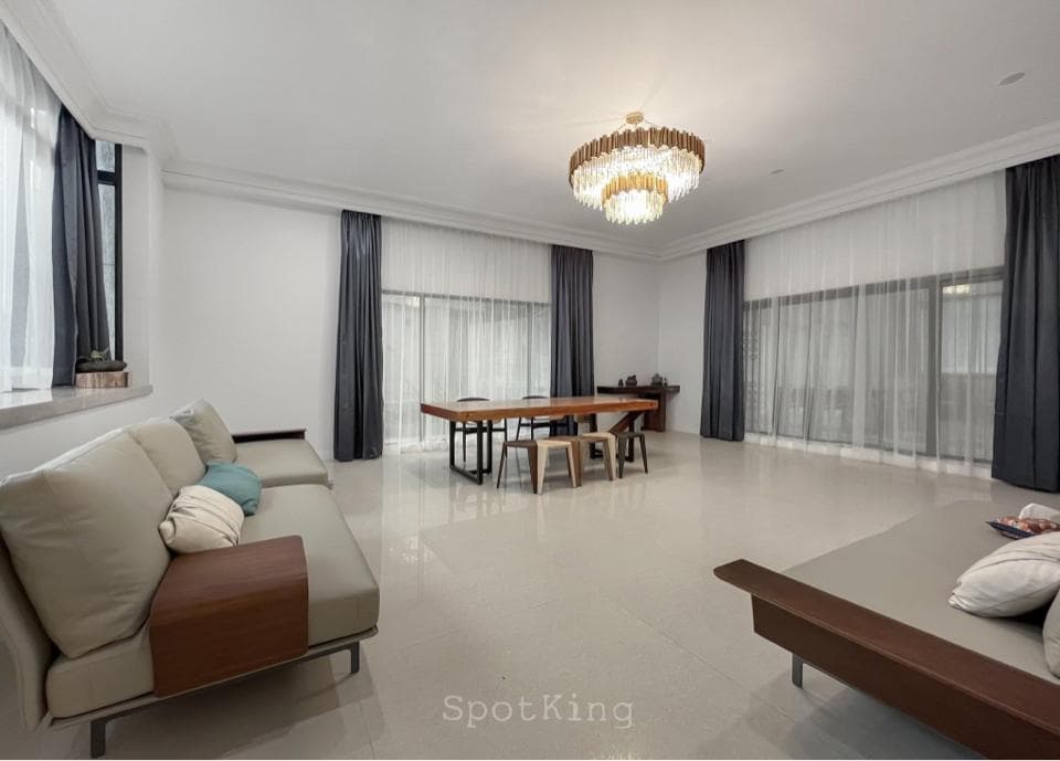 這張「現代風格客廳」的照片是,一個寬敞明亮的空間,帶有白色牆壁、淺色地板、窗戶上的薄紗窗簾,以及一個木質餐桌和沙發。 沙發旁有一張木質咖啡桌,上面放著一些裝飾品。 客廳中央懸掛著一盞時尚的吊燈,為空間增添了一份優雅的氣氛。