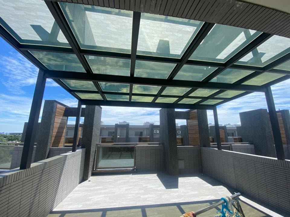 1) 照片顯示一個陽台,陽台上有玻璃屋頂,屋頂由黑色的金屬框架支撐,周圍是水泥牆