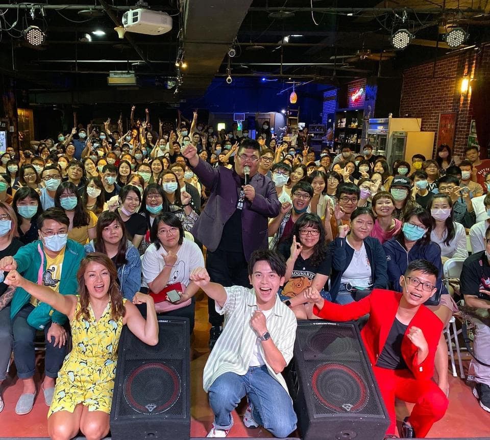 這張「一群人聚在一起」的照片是,一群人在一個室內場地,似乎在舉辦一個活動,中間站著一個穿著深色西裝的主持人,他正對著人群說話,臺下的人們都聚精會神地聽著。