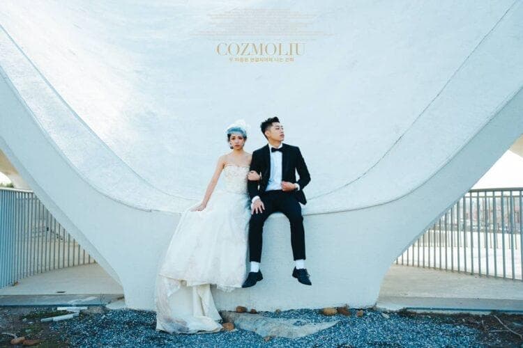 這張「婚紗照」的照片是 一對新人坐在白色的建築物上,新娘穿著白色婚紗,新郎穿著黑色西裝,背景是白色的建築物和藍色的天空。