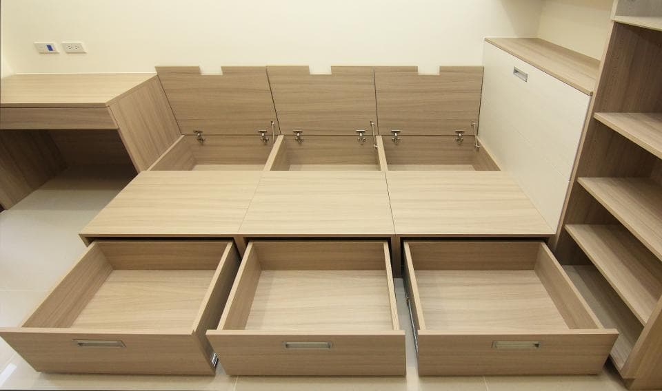 這張照片是一張床,床頭櫃上放了一個白色的抽屜,床底下有三個抽屜,其中一個抽屜是打開的。