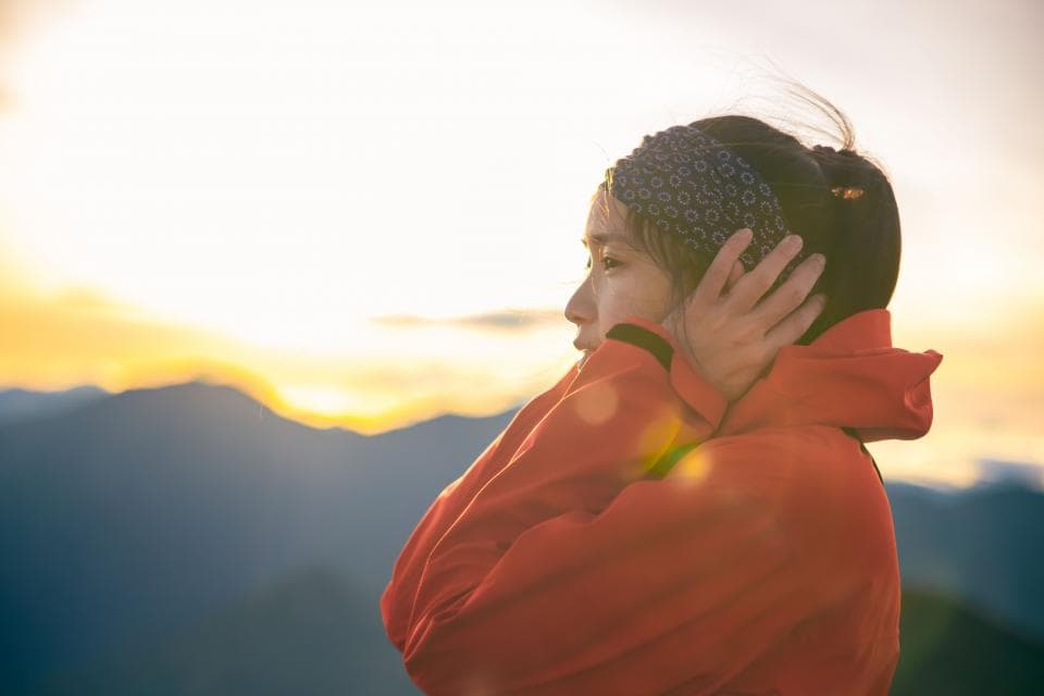 這張「一個女人站在山丘上,面朝夕陽」的照片是。她穿著一件紅色的外套,戴著一個黑色的頭帶,看起來很孤獨。