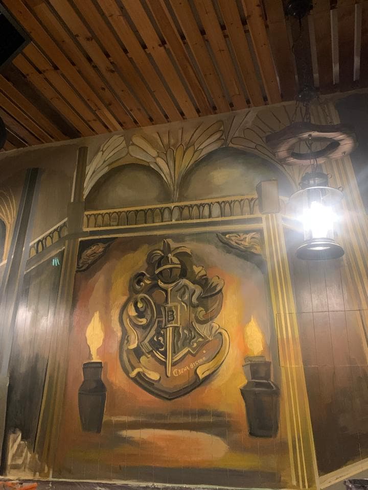 這張「霍格華滋」的照片是一面牆上繪製的霍格華滋的徽章,徽章旁邊有兩根蠟燭,牆壁的頂部是木製的天花板。