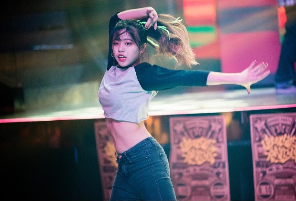 1) 照片顯示一位年輕女子身穿白色上衣和藍色牛仔褲,站在舞台上,正在跳舞