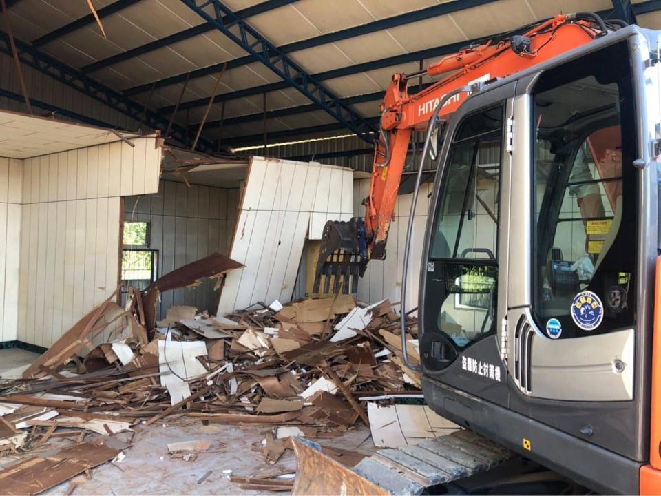 1) 照片顯示一台橙色挖掘機正在拆除一棟建築物