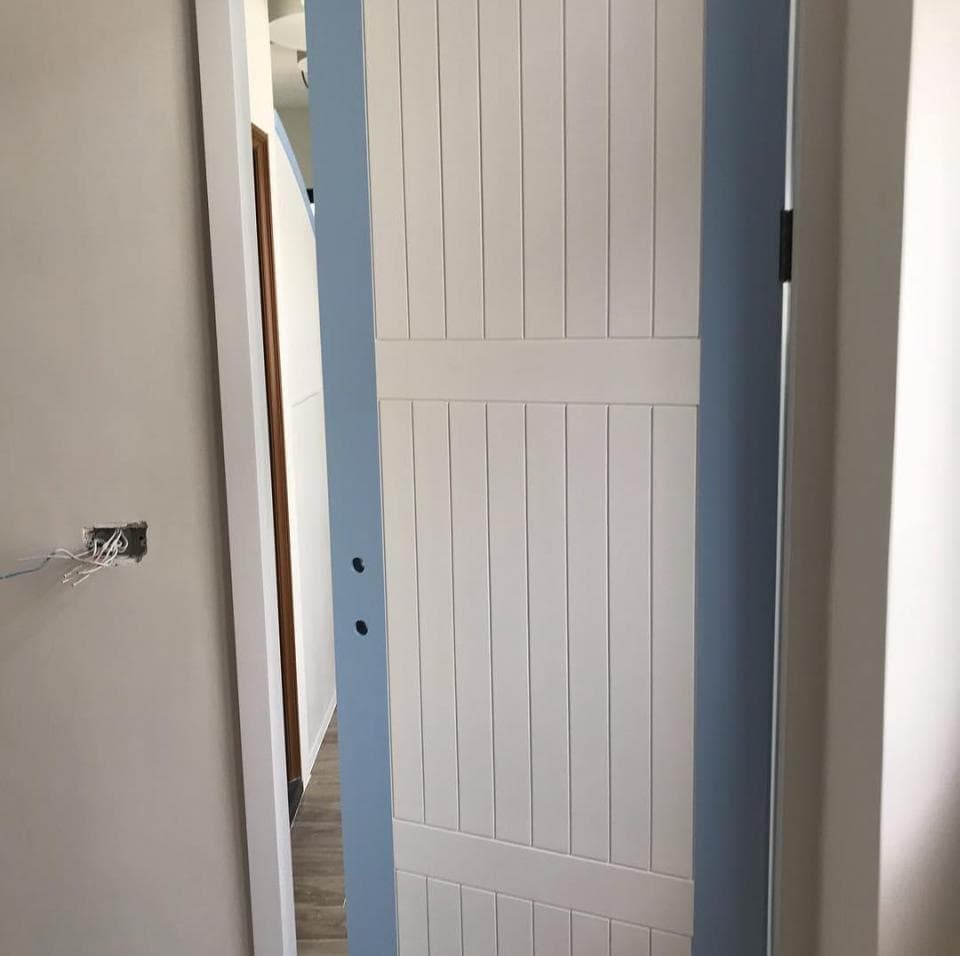 1) 照片顯示一個白色木門,門上有藍色的邊框,門上有水平的木條,門的左邊是一個白色的牆壁,牆壁上有一個電線盒