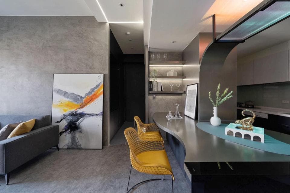 這張「現代風格住宅」的照片是,客廳以灰色牆面和抽象畫作為主,廚房則以不鏽鋼材質打造,並配有黃色椅子和綠色植物,呈現時尚簡約的風格。