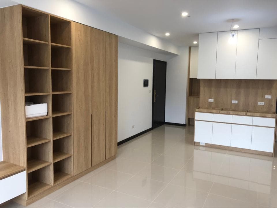 這張照片是一個現代化的客廳,主要特色是左側的木製層架和右側的白色櫥櫃。層架上有許多隔板,可以放書、擺飾或其他物品,而櫥櫃則可以收納各種物品,整體設計簡約而時尚。