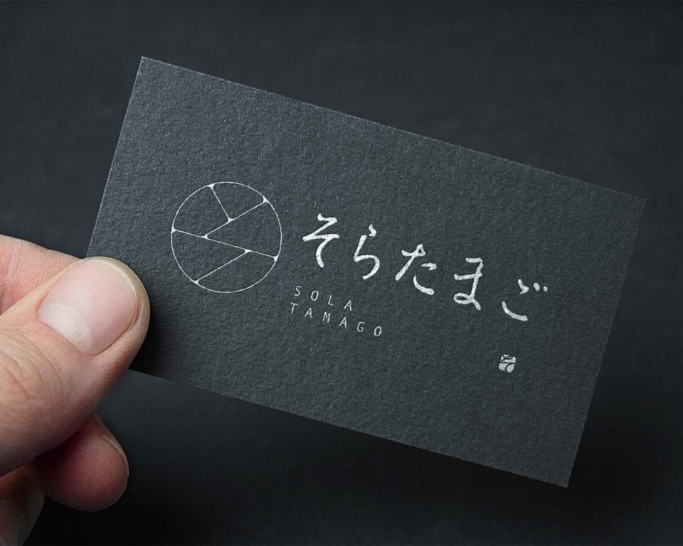 這張照片是一張黑色名片,上面有一個白色圓形圖案和日文文字 そらたこ。圖案像一個攝影鏡頭,有幾條線條分割成多個部分。