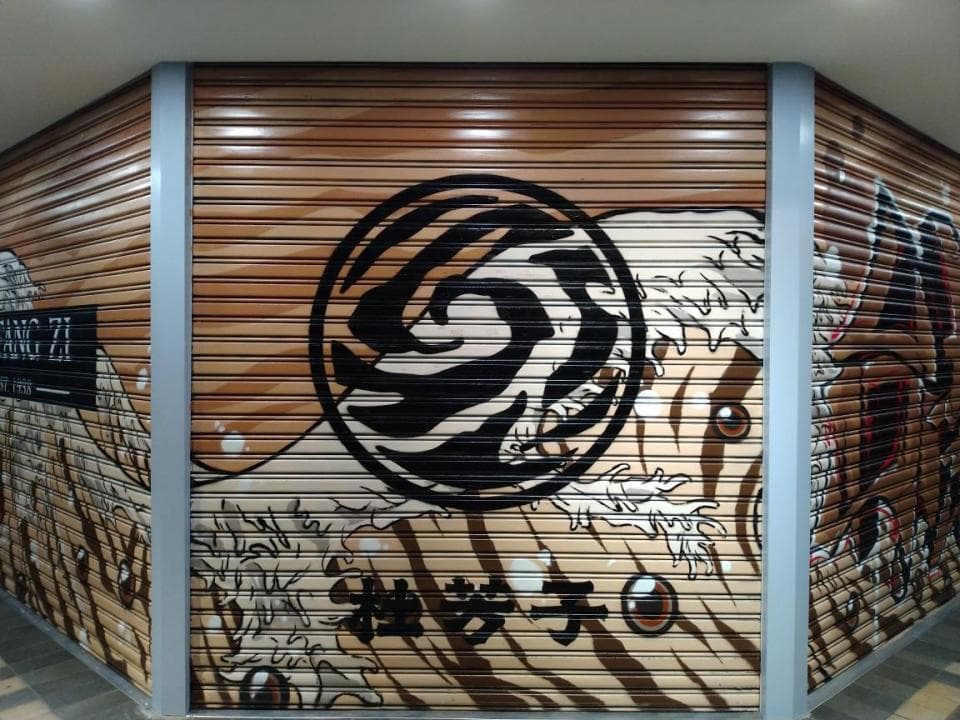 這張「卷閘門」的照片是,一個大的圓形圖案在卷閘門上,圖案裡面畫著一個海浪,旁邊還有其他圖案。