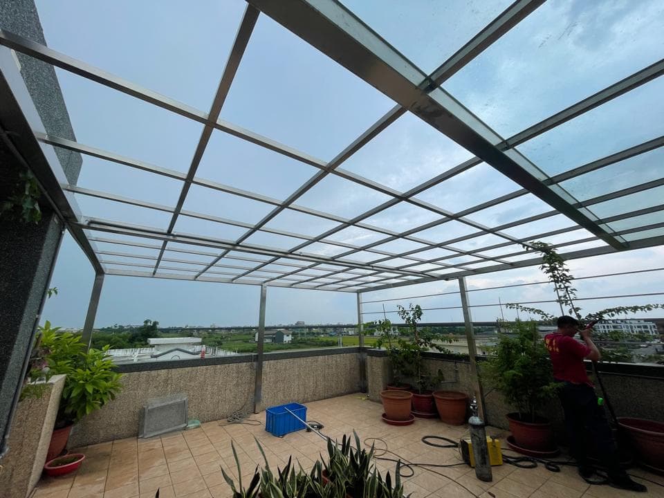 這張「陽臺」的照片是一個有玻璃屋頂的陽臺,陽臺上有許多植物和花卉,還有一個人在陽臺上工作。