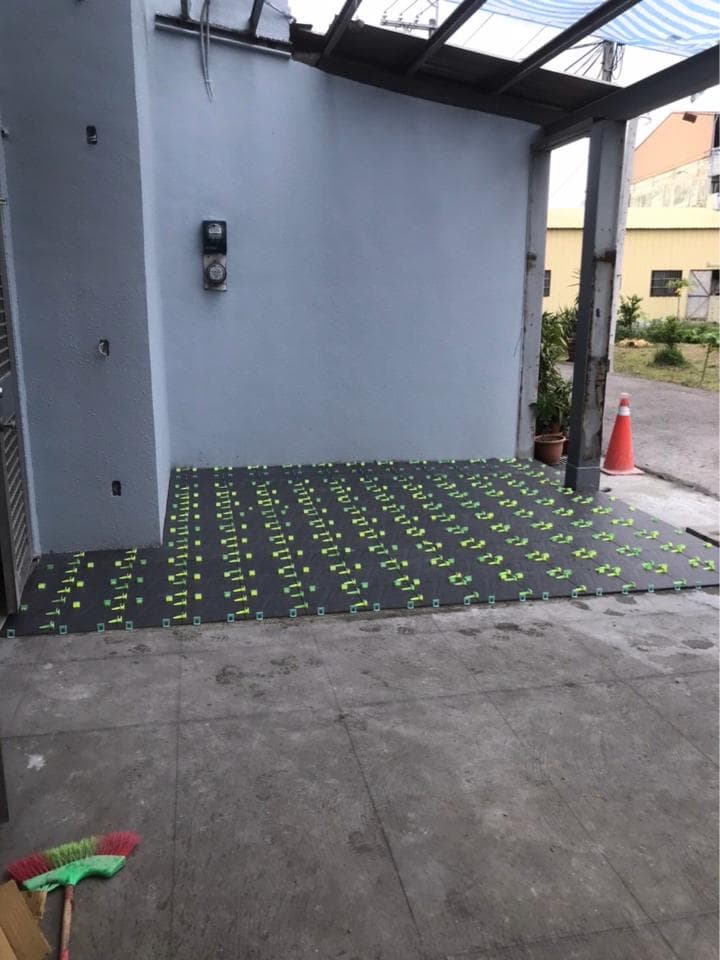 1) 照片顯示一個水泥地坪,上面鋪設黑色防水布,並使用黃色固定器固定
