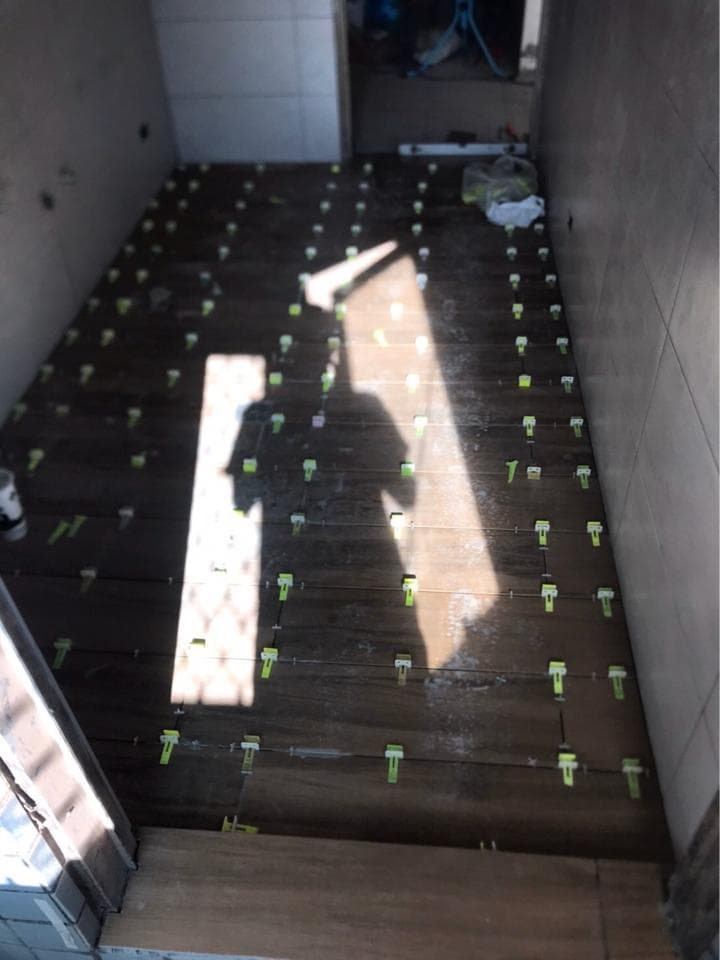 1. 照片顯示一個正在鋪設的木地板空間,地板上裝滿了綠色的瓷磚夾,地板上有光影