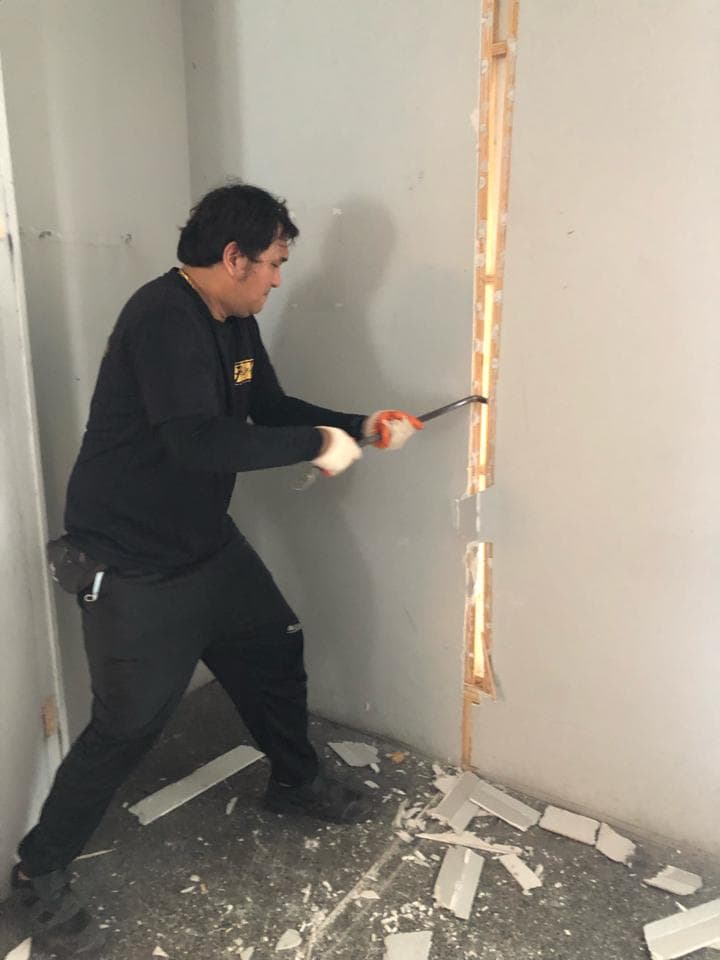 一名身穿黑衣的男子正在使用工具拆除牆壁上的木條