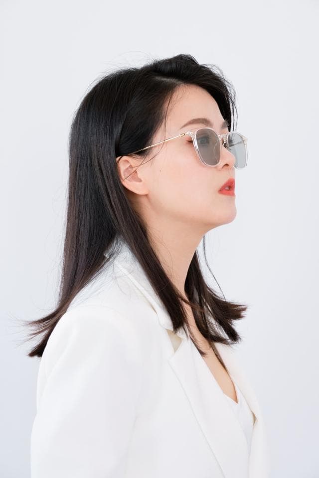 這張照片是一個戴著太陽眼鏡的年輕女子。她穿著白色的西裝外套,頭髮烏黑亮麗,散發著自信和時尚的氣質。