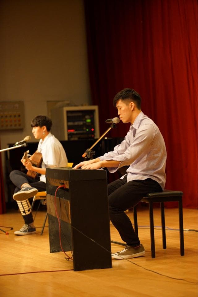 這張「兩個人在舞臺上表演」的照片是,一個男生彈著電子琴,另一個男生在旁邊彈著吉他。