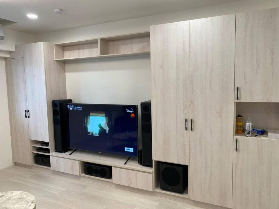1) 這是一張客廳的照片,裡面有一個木製的娛樂中心,中心擺放著一台平板電視、一組喇叭和一個重低音喇叭,電視櫃的下方有一個抽屜,娛樂中心旁邊有一個大的儲藏櫃