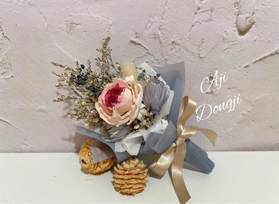 這張「乾燥花束」的照片是一束以粉色玫瑰為主的乾燥花束,搭配了其他乾燥花材,並以淺灰色包裝紙包覆,並以金色緞帶綁成蝴蝶結。