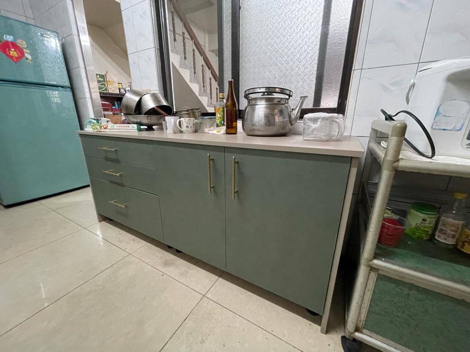 這張照片是一個廚房櫥櫃,櫥櫃的顏色是淺綠色,並且有金色把手。櫥櫃的材質看起來很光滑,櫃門上有一個金色的把手。