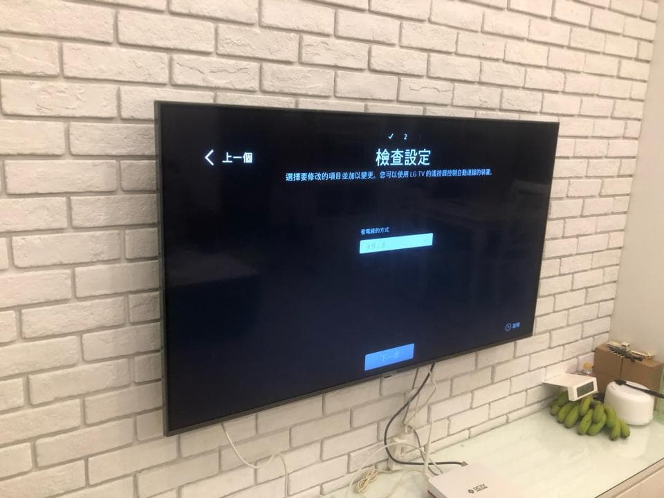 1) 照片顯示一臺安裝在白色磚牆上的黑色電視,電視螢幕上顯示著設置選單,選單中有「檢查設定」的標題和一個輸入框