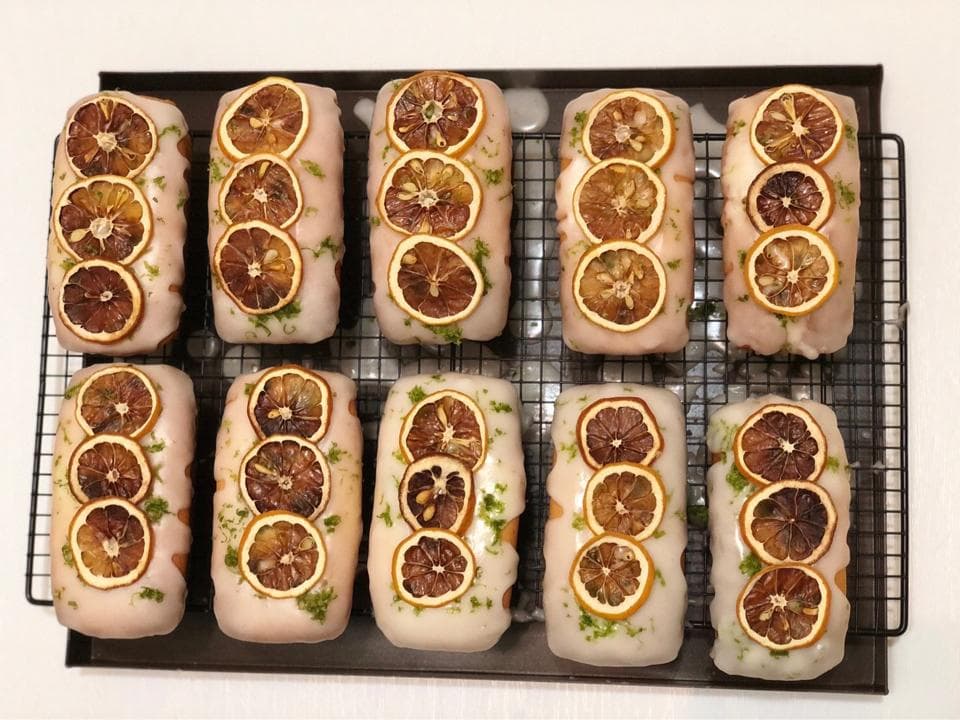 這張照片是九個裝飾著柑橘片的蛋糕,蛋糕上鋪著白色糖霜,放置在金屬架上。