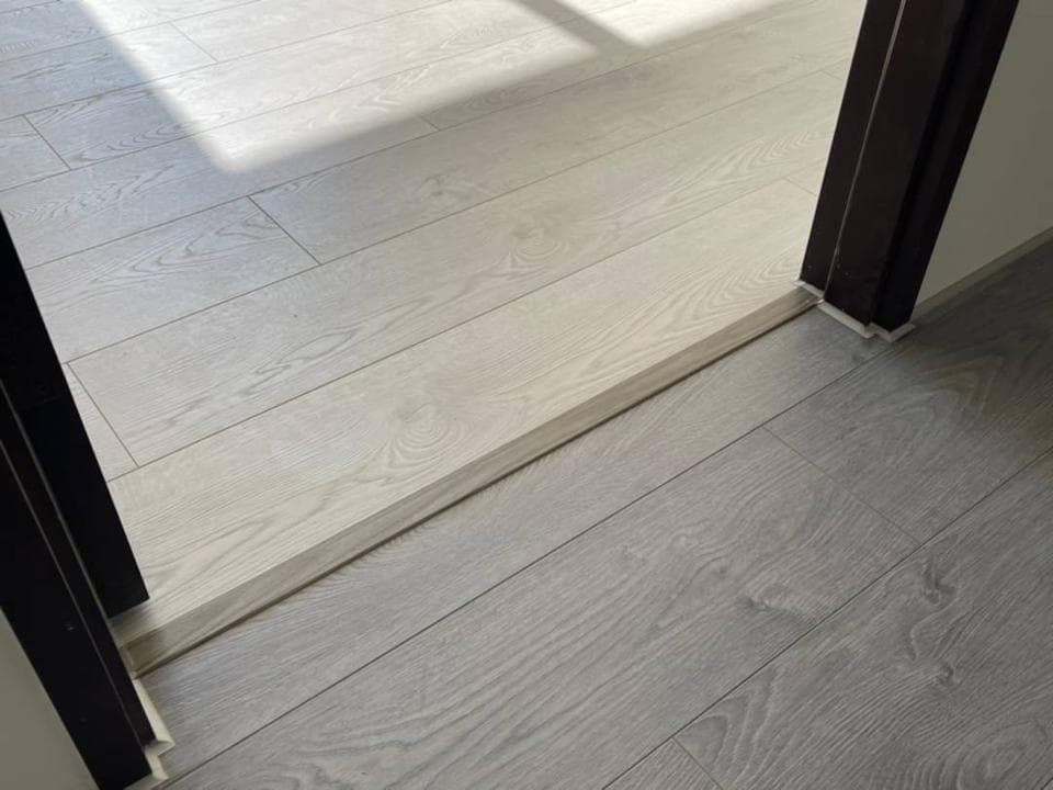 1) 照片顯示了一個房間裡鋪設好的淺灰色木地板,其中一側有門,門邊有條過渡條