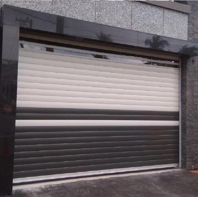 這張照片是一扇雙色電動捲門,上半部是白色,下半部是灰色,中間有一條白色橫條。捲門上有許多細小的橫條,看起來很有質感。