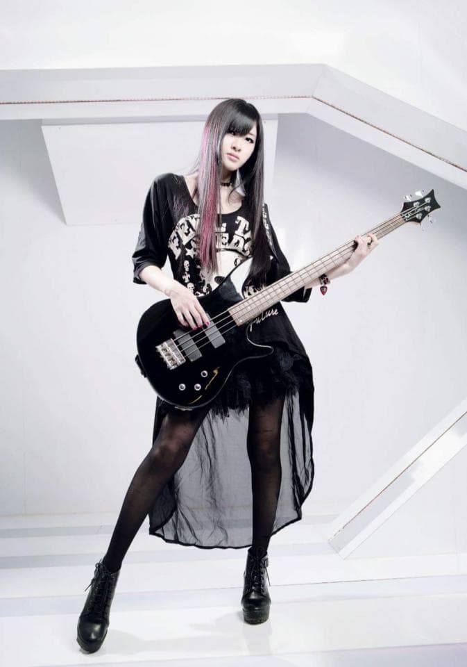 1) 照片中是一位穿著黑色長裙,黑色網襪,黑色靴子,黑色上衣的女性,手持一把黑色貝斯,站在白色背景下
