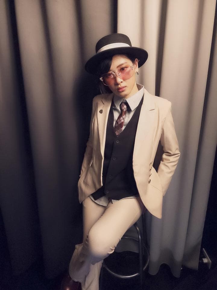 這張「一個穿著西裝和帽子、戴著太陽眼鏡的年輕人站在背景牆前」的照片是。