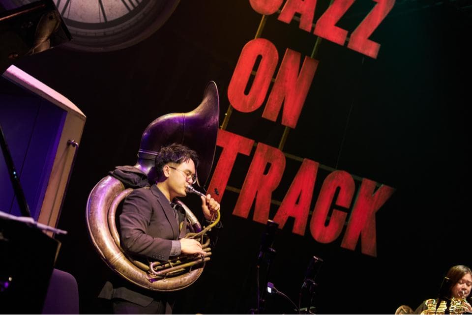 這張照片是一個爵士樂手正在演奏大號。他專注地吹奏著樂器,他的表情充滿熱情和投入。 他的樂器是一支巨大的大號,看起來很專業,也展現出他的音樂技巧。