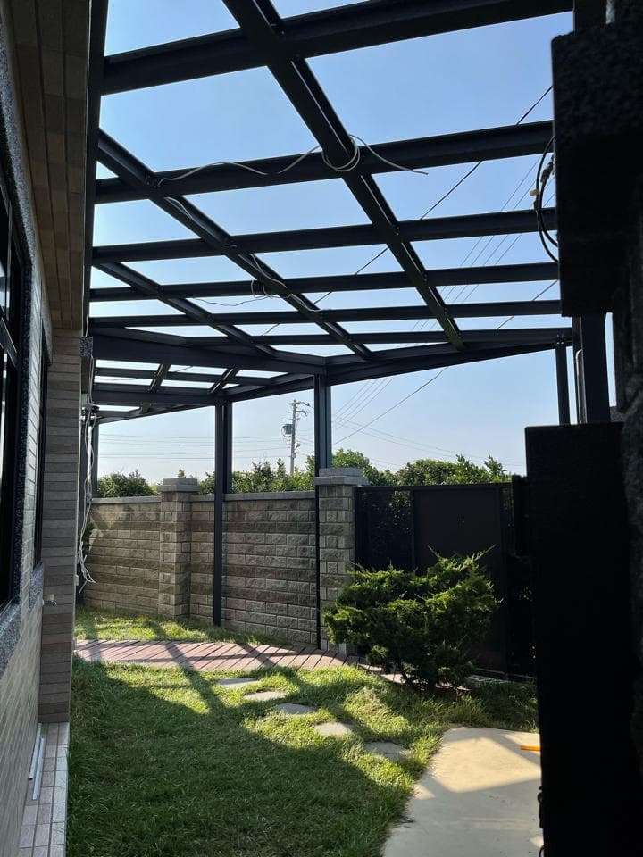 這張照片是一個帶有玻璃屋頂的陽臺,陽臺上有水泥砌成的矮牆,牆外種植了綠色植物,陽光透過屋頂照射在綠地上,形成斑駁的光影。