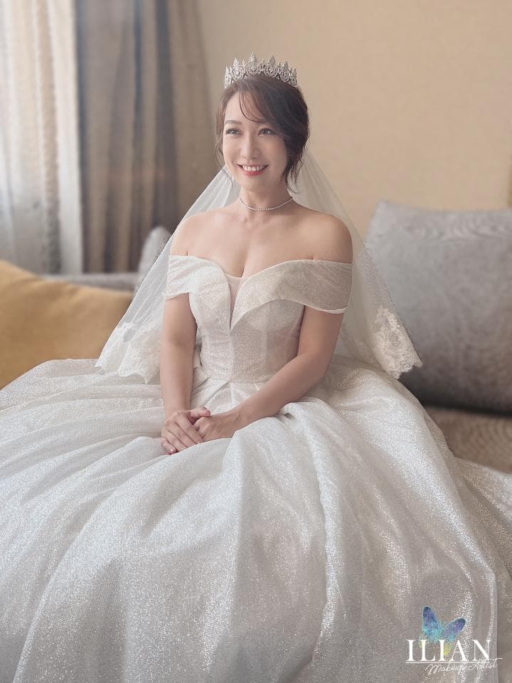 這張照片是一個穿著婚紗的新娘坐在沙發上。她戴著皇冠,笑容燦爛,看起來非常幸福。