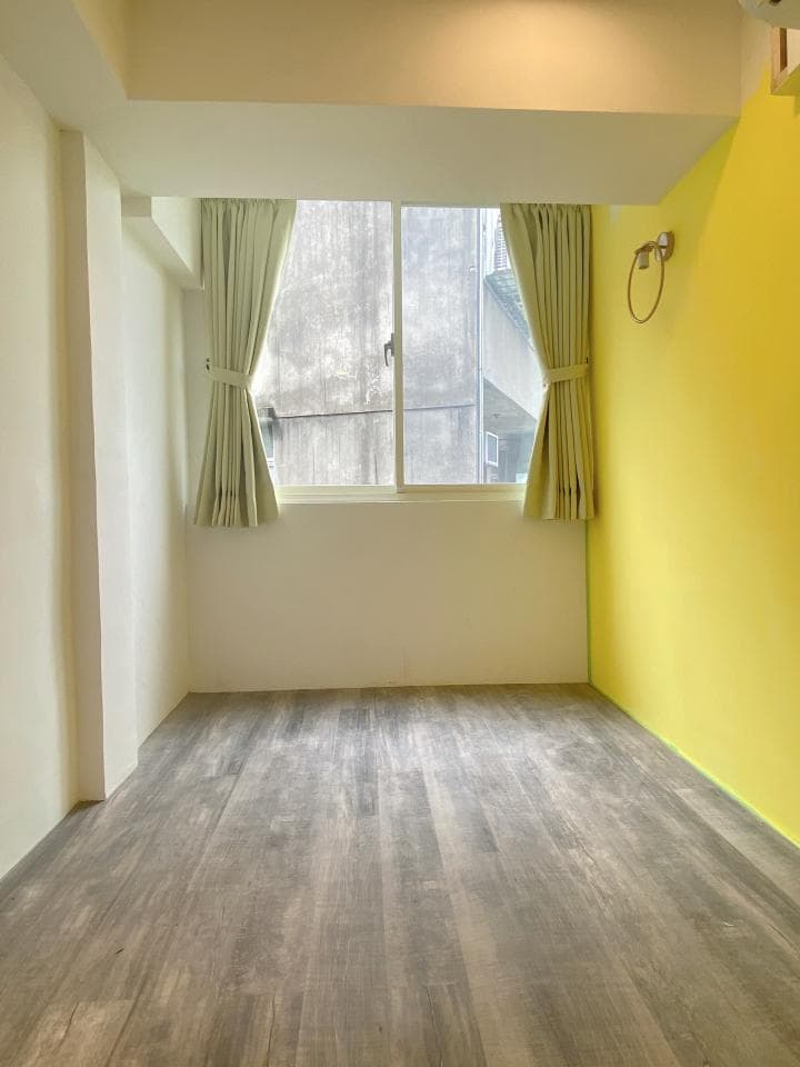 1) 這是一張室內照片,拍攝角度為室內一角,照片中可以看到一扇窗戶,窗戶上裝有白色窗簾,窗戶外的風景是附近建築物的外牆,牆壁上有黃色油漆