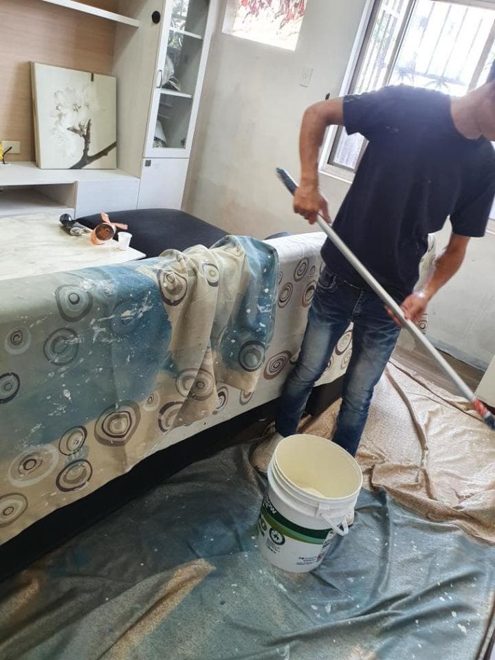 這張照片是一名男子正在用滾筒刷油漆,他正在刷一堵牆,牆上已經塗了一層白漆。