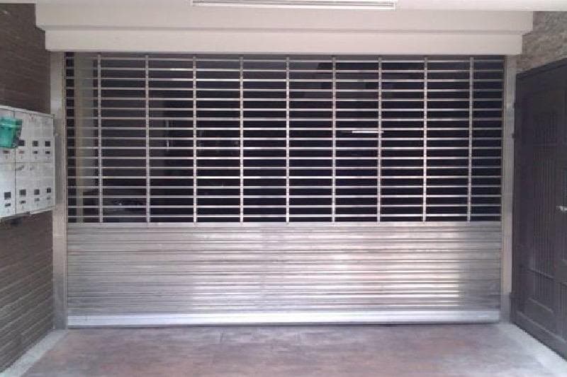 這張照片是一個金屬捲門,它是由許多水平的格柵組成,並且可以上下捲動。捲門看起來是新的,而且被安裝在一個牆上,並且用來封閉一個入口。