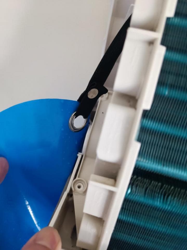 1) 照片顯示一個藍色塑膠布正在被拉開,露出下方一個白色機器的散熱器