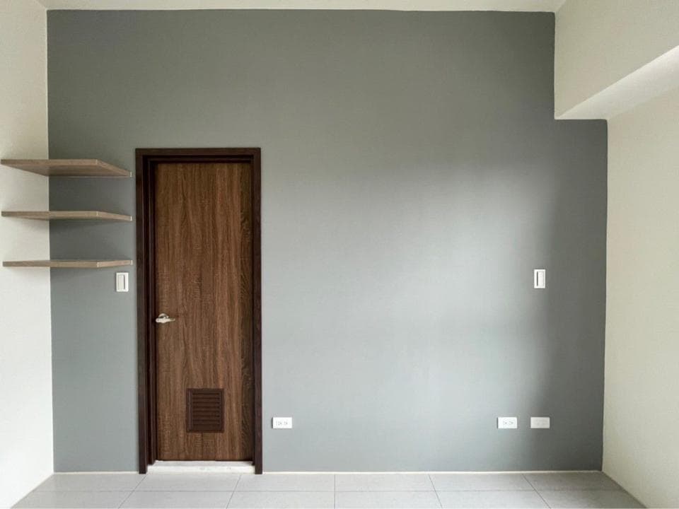 1) 照片顯示一間空房間,牆壁是灰色,房間裡有一個木門,牆壁上有三個架子,牆壁上有三個開關