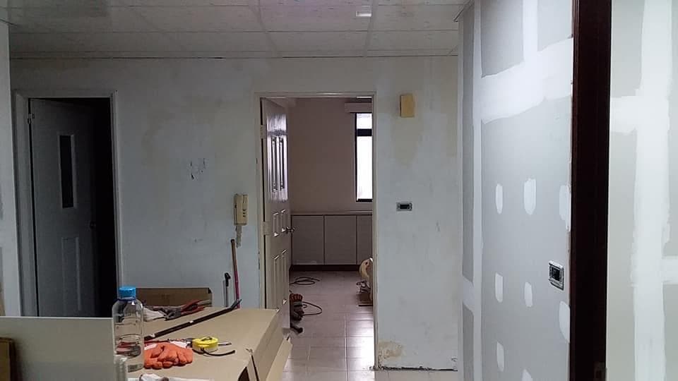 這張照片是一個正在裝修的房間,房間裡牆壁上有很多補土的痕跡,看起來正在進行粉刷的步驟,牆壁上有一個開關。